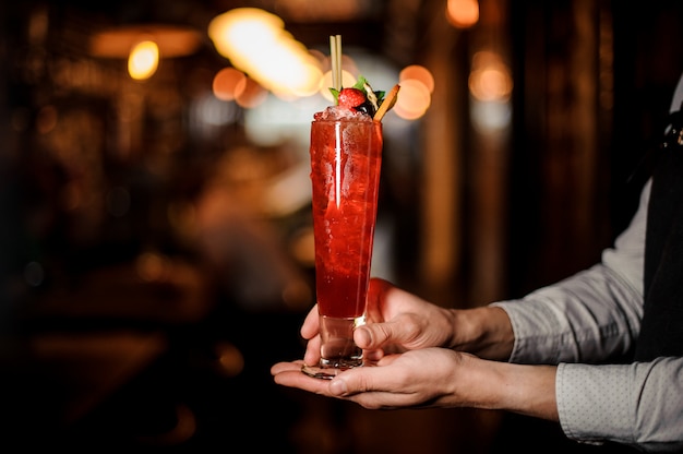 Professional bartender holding a delicious red cocktail in the glass