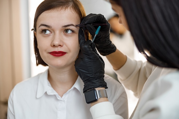 Professional brow master is doing her job for beautiful woman at beauty salon