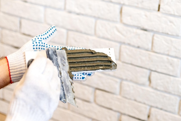 A professional builder sticks decorative tiles on the wall A worker mounts a decorative brick on a wall