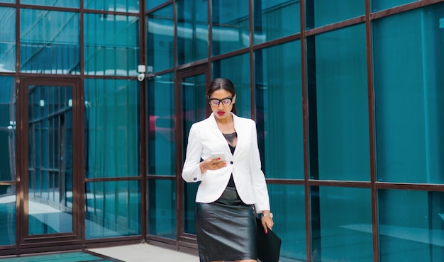 Professional business afro woman in elegant white jacket and skirt with folder with documents in her hands  use smartphone