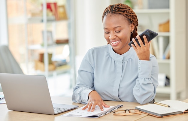 Professional business woman with phone call reading notebook on her laptop computer in modern office Woman corporate employee sitting at desk talking on smartphone at table in a startup company