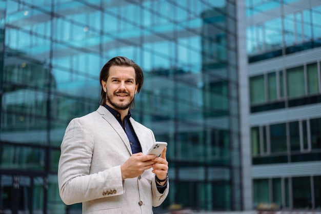 Professional businessman in suit looking at camera while standing on street with mobile phone App