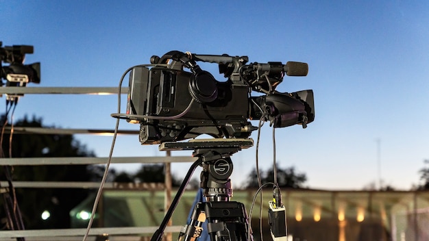 A professional camera on a tripod with a lot of cables at dusk