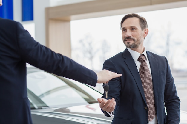 Professional car dealer passing keys to his customer new car owner