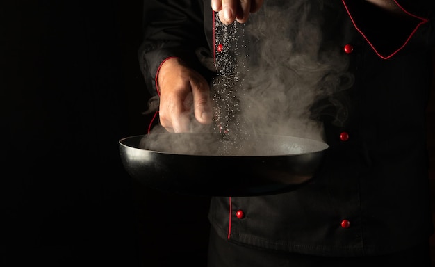 Professional chef adds salt to a hot pan with meat burger cutlets