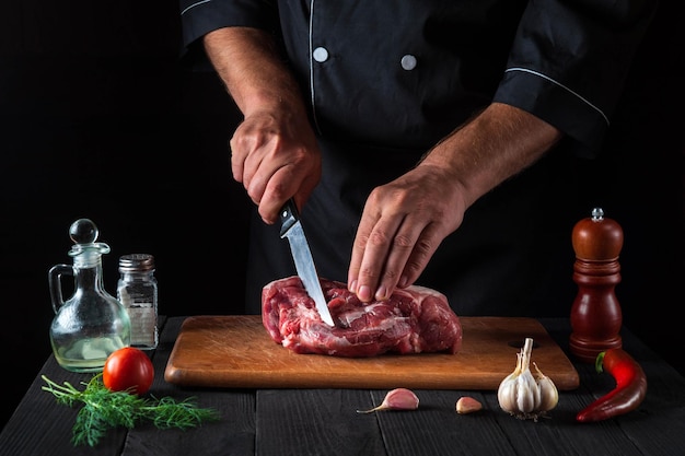 Professional chef cuts meat with a knife in the kitchen prepares food Vegetables and spices