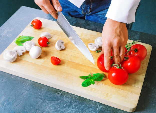 Professional chef cuts vegetables with a sharp knife from Damascus steel. Mixed media