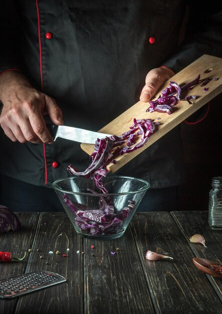 A professional chef pours red cabbage into a bowl Cooking vegetable salad in the restaurant kitchen