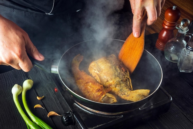 Professional chef prepares fish in the restaurant kitchen. Boil or fry crucian carp in a pan. The idea of a delicious fish diet.