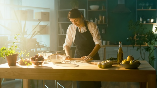 Professional chef sprinkles flour and kneads dough on a wooden table startup