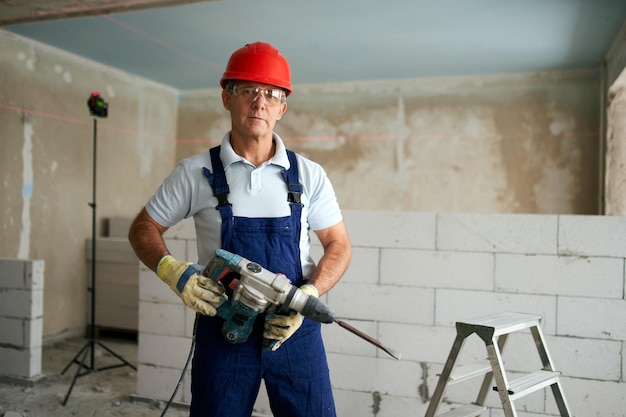 Professional construction worker in uniform standing with rotary hammer drill portrait of contractor