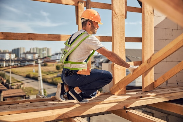 Professional constructor wearing helmet while preparing frame for covering roof on the future house