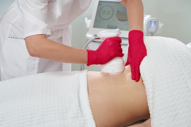 professional cosmetologist performing radiofrequency lifting procedure on the stomach of a woman