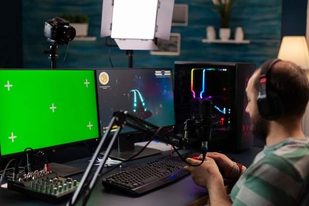 Professional cyber streamer playing digital videogames on professional powerful computer with green screen display. Player using pc with mock up chroma isolated desktop streaming shooter games