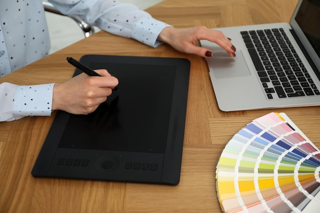 Professional designer with graphic tablet at wooden table closeup