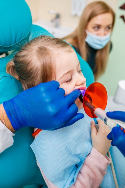 A professional doctor, a children's dentist, treats a little girl's teeth with instruments. Dental office for patient examination. The process of dental treatment in a child