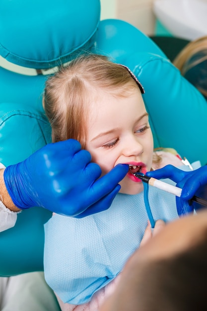 A professional doctor, a children's dentist, treats a little girl's teeth with instruments. Dental office for patient examination. The process of dental treatment in a child