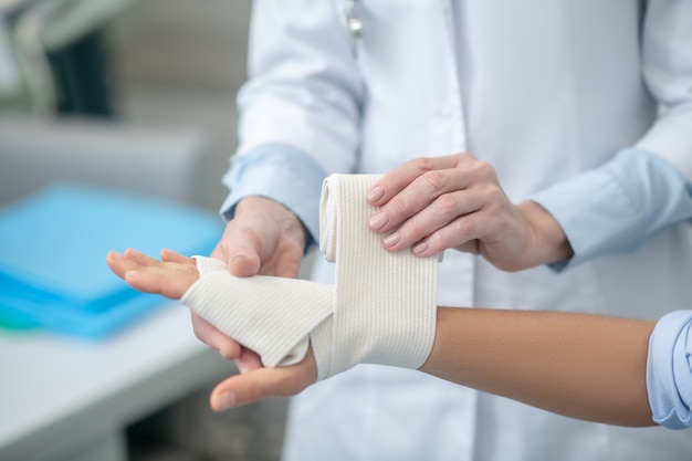 Professional doctor hands bandaging fixing palm of patient in hospital, faces are not visible