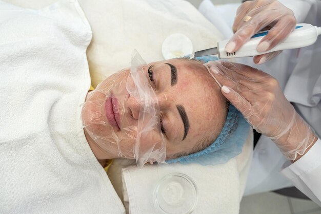 Professional female cosmetologist in a mask makes facial contour injections to female patient