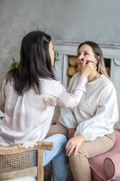 Professional female makeup artist applying cosmetics on model face use brush working at beauty salon