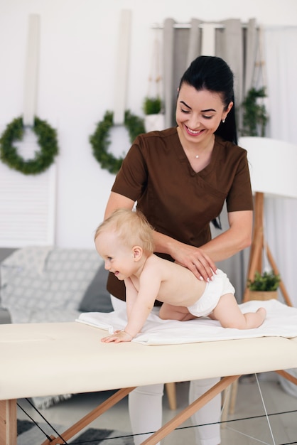 A professional female masseuse makes a massage to a little baby. Children's massage on the couch in a modern cozy room.