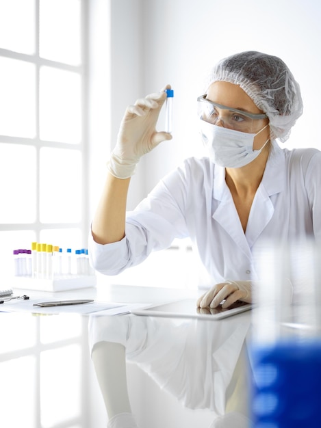 Professional female scientist in protective eyeglasses researching tube with reagents in laboratory. Concepts of medicine and research.