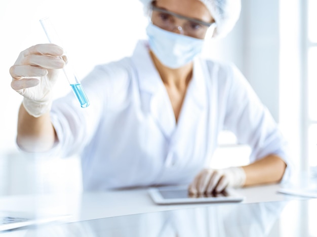 Photo professional female scientist in protective eyeglasses researching tube with reagents in laboratory. concepts of medicine and science researching.