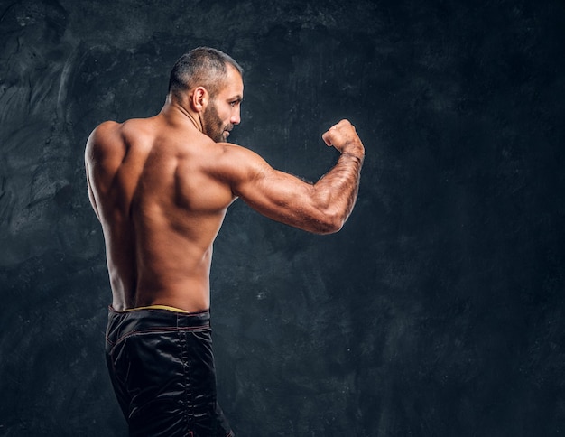 Professional fighter showing kick fighting technique. Studio photo against a dark textured wall