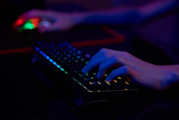 Professional gamer play computer video game in dark room use neon colored rgb mechanical keyboard place for cybersport gaming