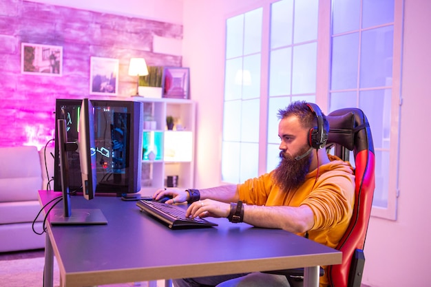 Professional gamer with long beard in front of powerful gaming rig in room full of neon lights