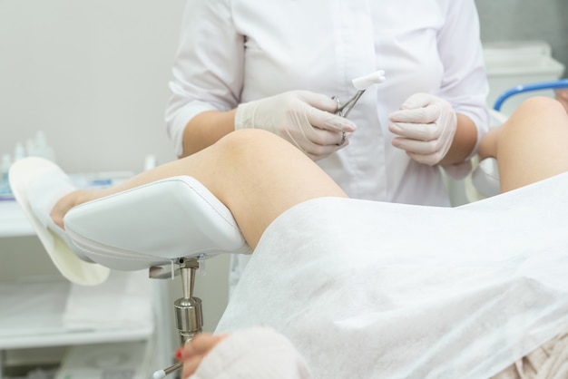 Professional gynecologist examining female patient on gynecological chair holding forceps