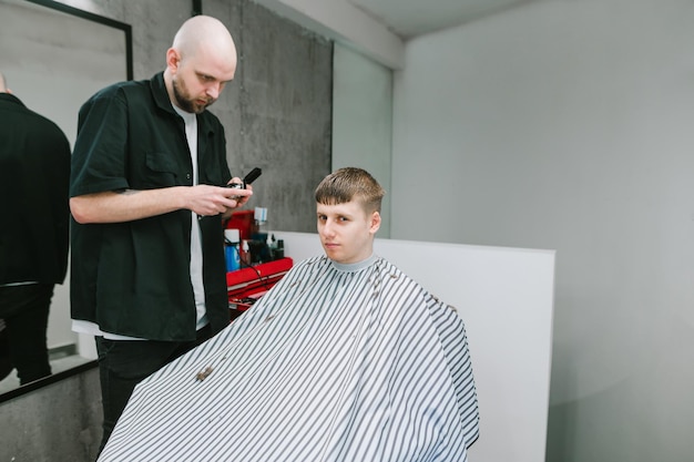 Professional hairdresser cuts a young man with a clipper and a comb in his hand