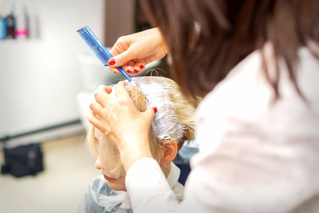 Professional hairdresser dyeing hair of her female client in white color at hair salon