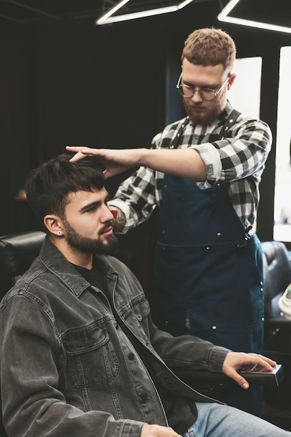 Professional hairdresser working with bearded client in barbershop