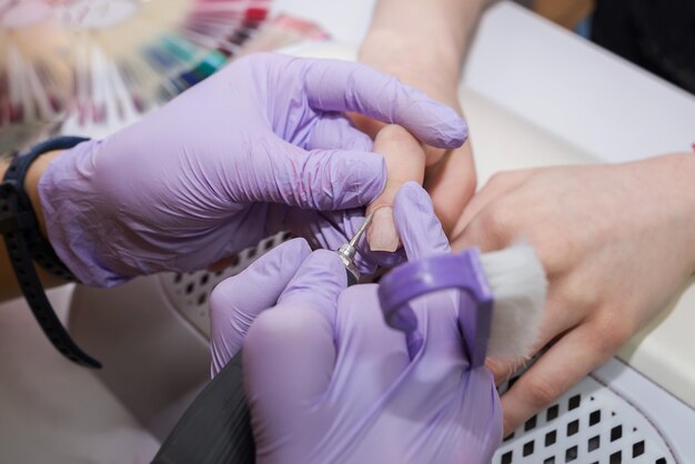 Professional hardware manicure on an electric machine in a beauty salon. The master uses an electric machine to remove nail polish from his hands during a manicure.