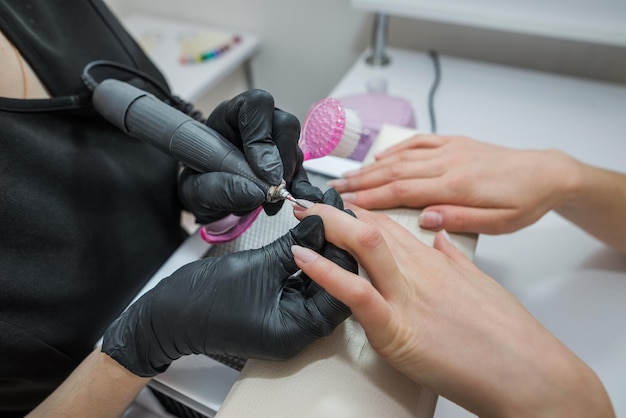 Professional hardware manicure on an electric machine in a nail salon The process of lifting the cuticle with a cutter closeup Master uses an electric nail file drill to trim and remove cuticles