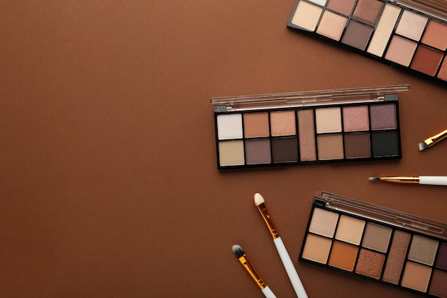 Professional makeup palette with brushes on brown background with copy space. Top view.