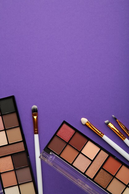 Professional makeup palette with brushes on purple background with copy space. Top view.