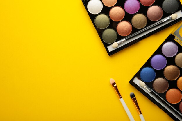 Professional makeup palette with brushes on yellow background with copy space. Top view.