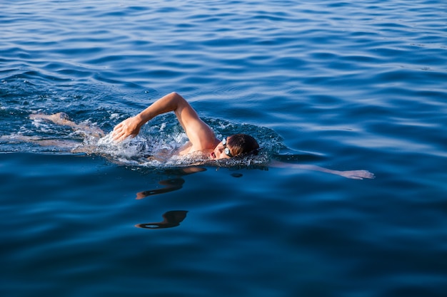 Professional male athlete swimming in clear blue water in sunlight.