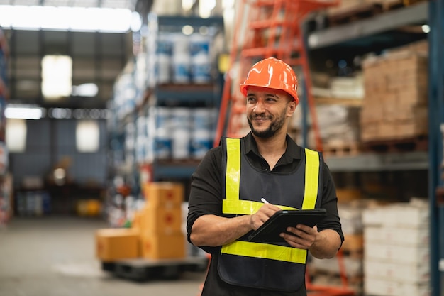 Professional manager man employee smile using tablet check stock working at warehouse Worker wearing high visibility clothing and a hard hat helmet and checking and count up goods boxes delivery