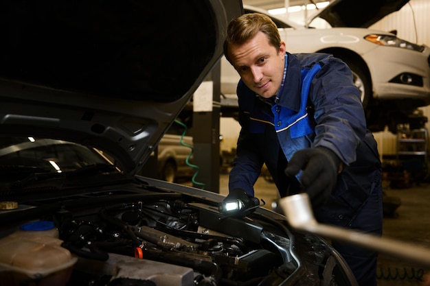 Professional mechanic, Caucasian man in overall work uniform examining tuning, fixing, repairing car engine, vehicle parts using tools equipment in workshop garage. Support and car repair service