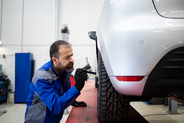 Professional middle aged bearded caucasian car mechanic doing visual inspection of braking pads and discs.