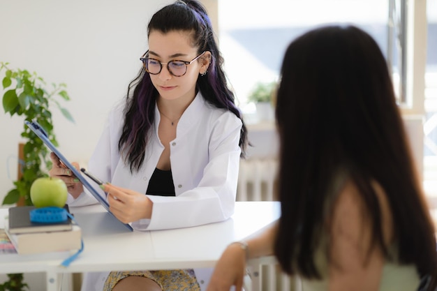 Professional nutritionist giving consultation about diet plan and healthy eating to help the patient loss weight Female doctor showing prescription to her client sitting in the office