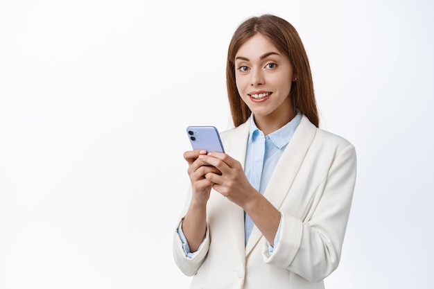 Professional office woman using mobile phone, wearing business suit, white wall