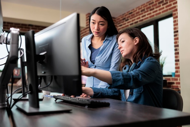 Professional office workers pointing out wrong blueprint of project while using work computer. Creative designers developing digital arts on PC while discussing about 3D technology.