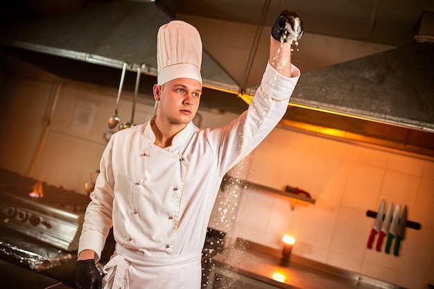 Professional pastry chef prepares dough with flour to make bread Italian pasta or pizza Flour is flying in the air on kitchen background Baking food concept