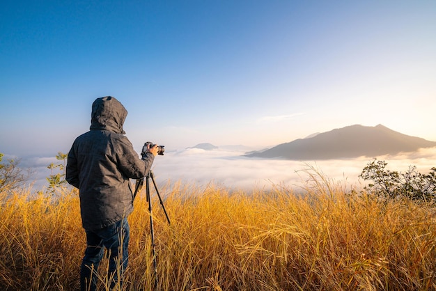 professional photographer taking a photo with camera lens on tripod with mountain sunset view