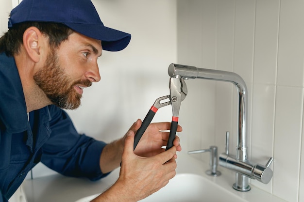 Professional plumber in blue uniform fixing broken water tap in kitchen repair service concept