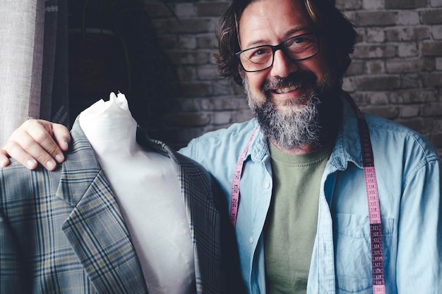 Professional portrait of tailor man smiling inside his workshop store embracing mannequin dummy Alternative job and people Happy male worker smile at the camera Tailoring activity Fashion industry